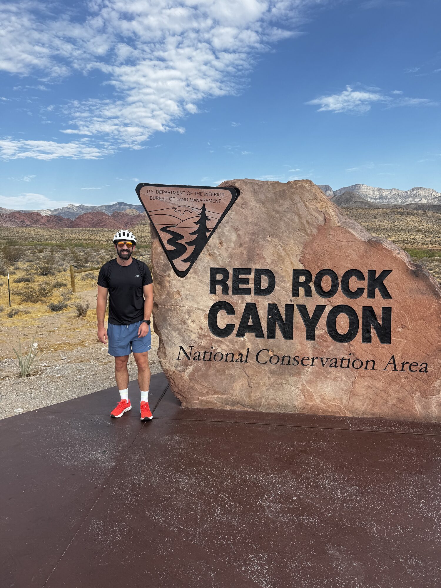 Standing at the Red Rock Canyon National Conservation Area sign in cycling gear
