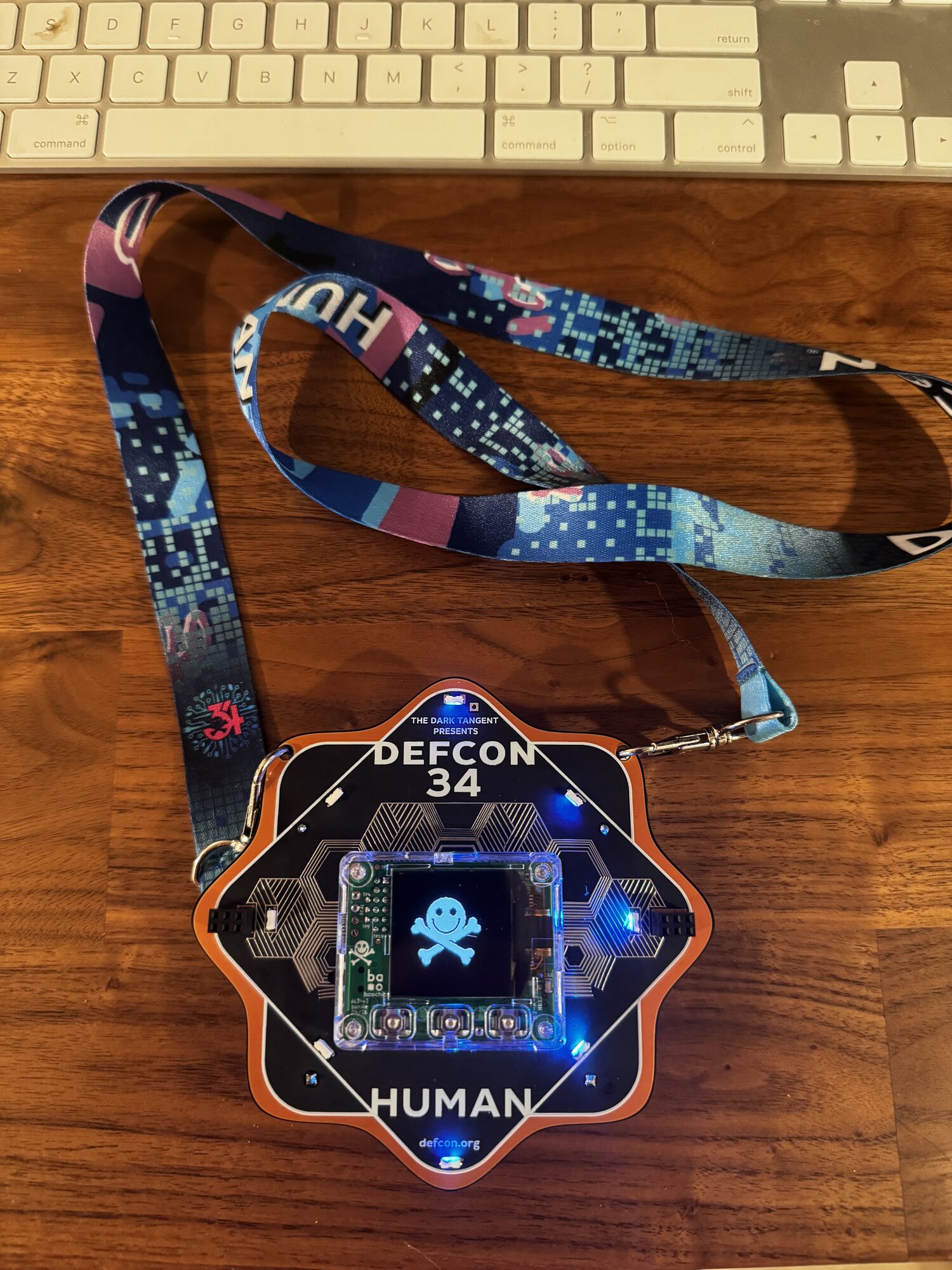 DEF CON 34 HUMAN badge with lanyard, screen showing a skull smiley
